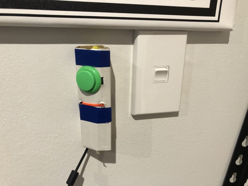 A green arcade button stuck to the wall next to a light switch